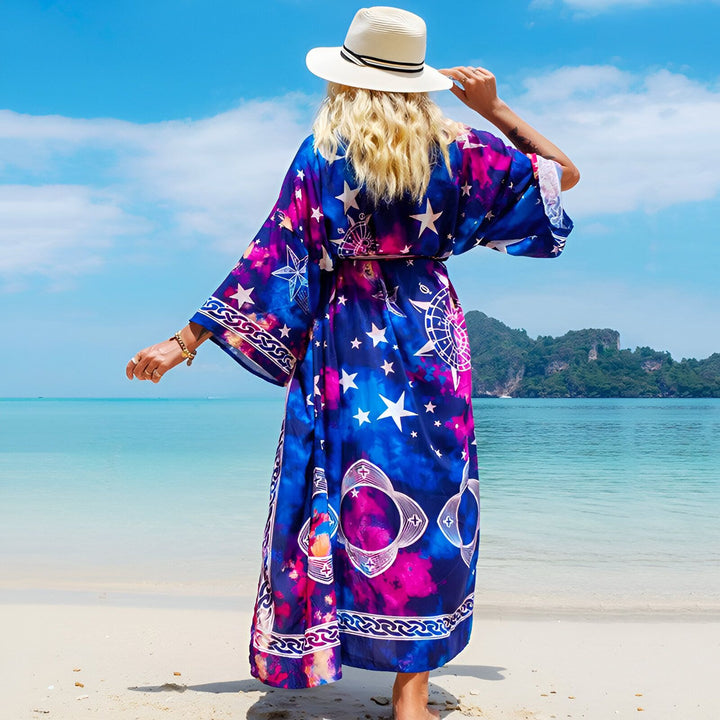 Femme portant un kimono long bleu et rose à motifs étoiles et boussole sur la plage. Kimono d'été élégant avec chapeau. Collection de kimonos pour femme.