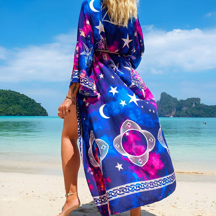 Femme portant un kimono coloré sur la plage. Le kimono est bleu, rose et violet avec des motifs d'étoiles et de lunes. Kimono d'été, vêtement de plage, mode féminine.