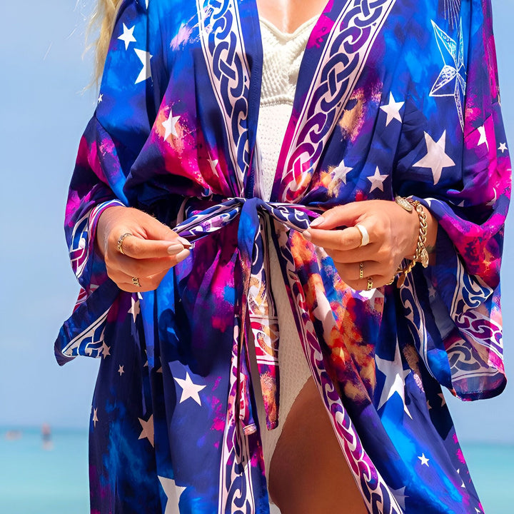 Femme nouant un kimono bleu et rose à motifs étoiles. Vêtement léger parfait pour la plage ou la détente. Notre collection de kimonos offre style et confort.