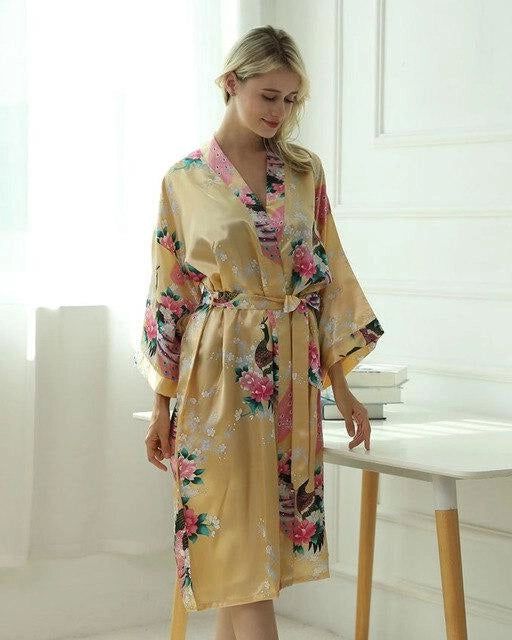 Femme portant un kimono doré à motifs floraux et de paon. Peignoir de style japonais à porter à la maison. Vêtements d'intérieur confortables et élégants.