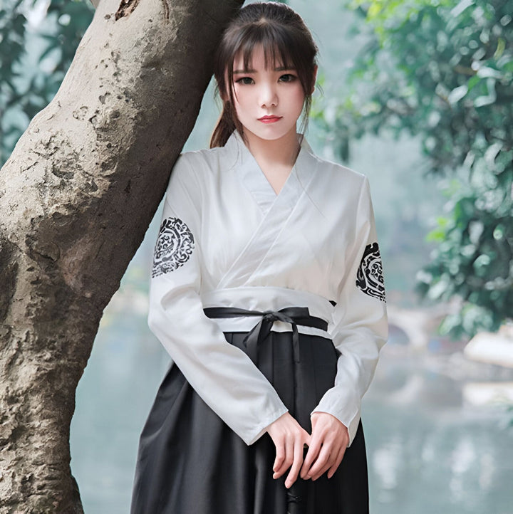 Jeune femme portant un kimono traditionnel blanc et noir, appuyée contre un arbre. Vêtements japonais à découvrir dans notre collection.