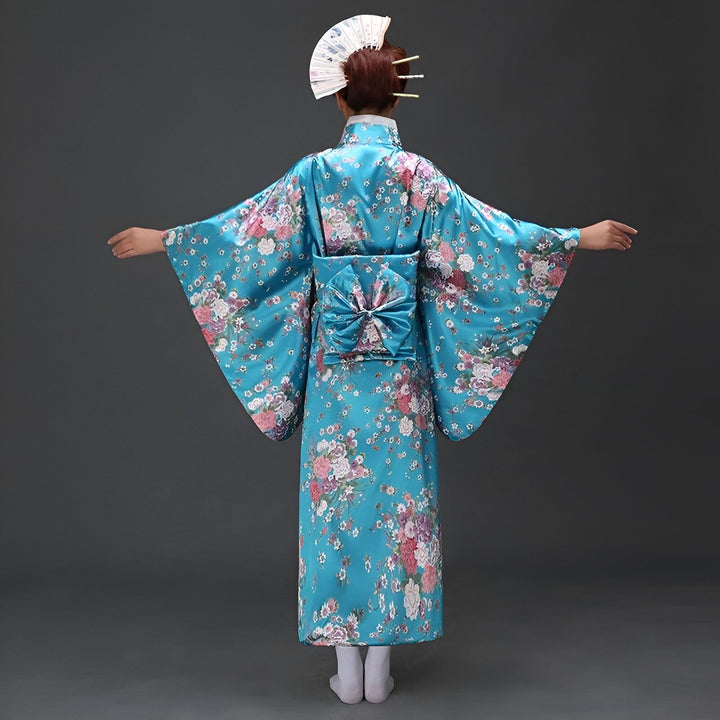 Femme portant un kimono traditionnel japonais bleu à motifs floraux. Vue de dos, elle a un éventail dans les cheveux et les bras écartés. Costume traditionnel, culture japonaise, mode asiatique.