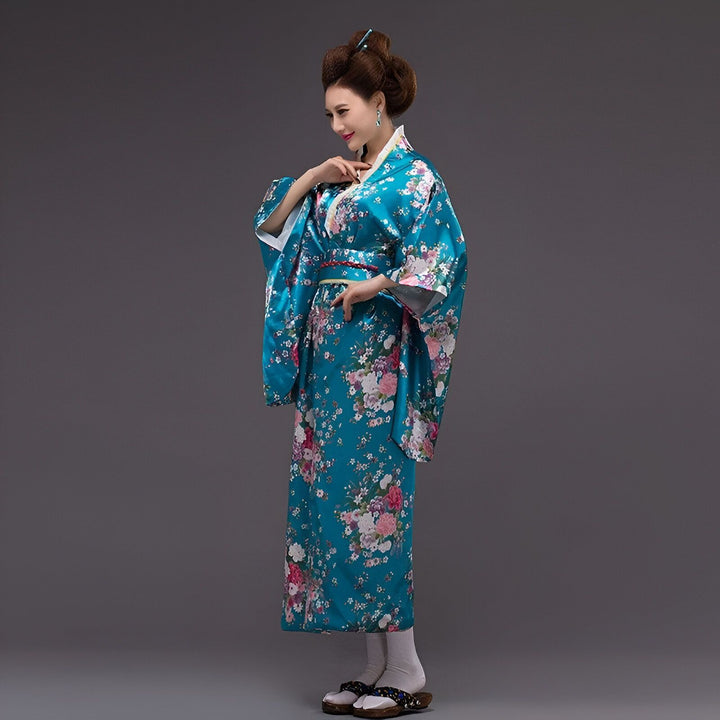 Une femme portant un kimono traditionnel bleu à motifs floraux colorés, des sandales en bois geta et les cheveux relevés en chignon.
