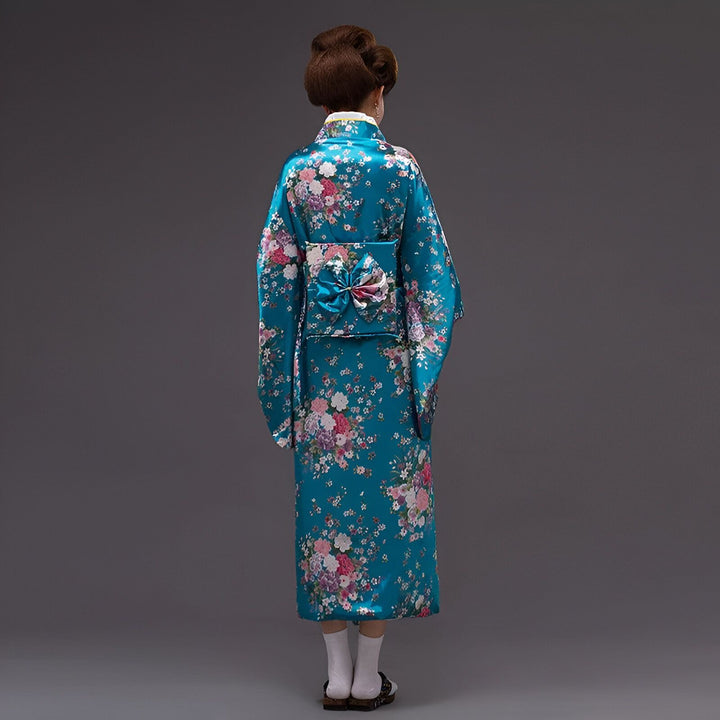 Femme portant un kimono bleu avec des motifs floraux. Vue arrière d'une personne en tenue traditionnelle japonaise, coiffure chignon, obi décoratif.