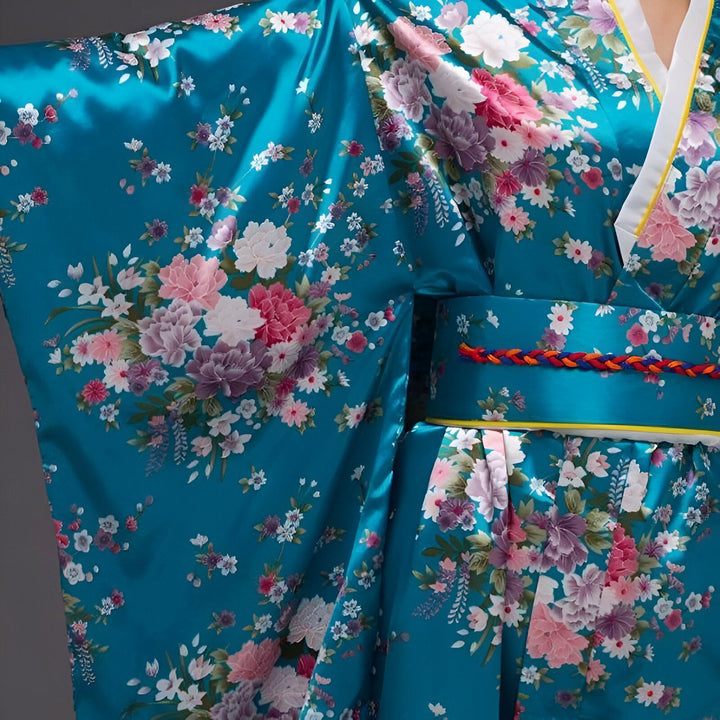 Kimono traditionnel japonais en soie bleue turquoise, orné de motifs floraux roses et blancs. Détails de la ceinture obi tressée et du col blanc. Élégance et raffinement de la culture japonaise.