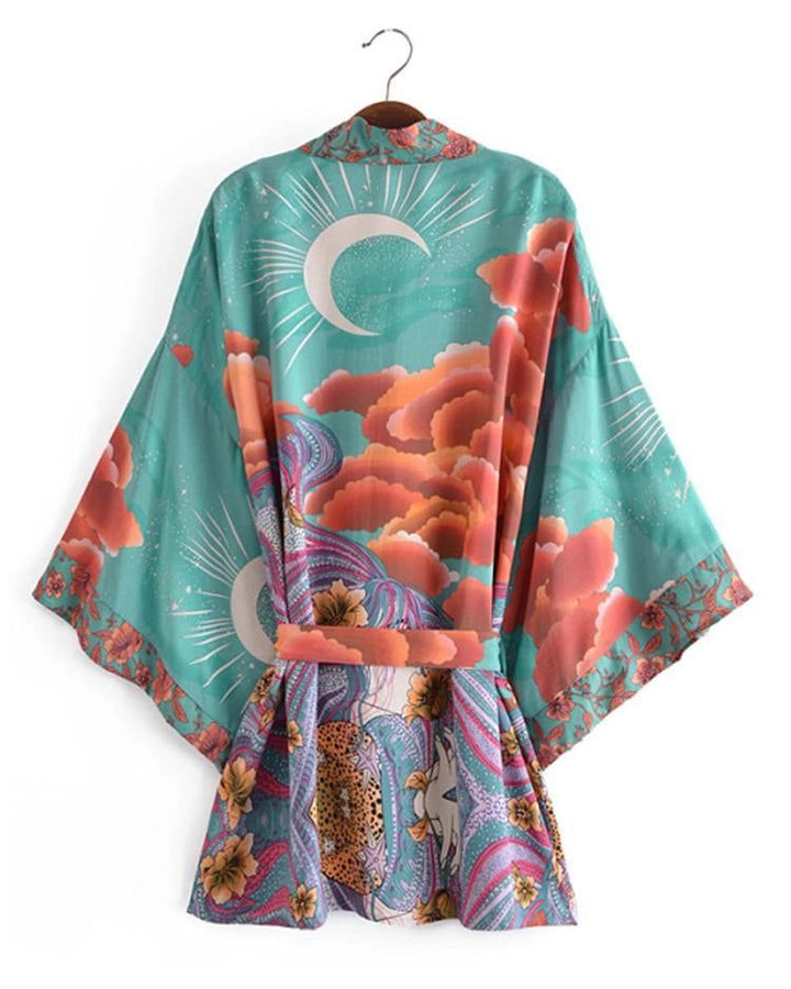 Kimono turquoise imprimé lune et nuages orange, suspendu sur un cintre. Vêtement ample et coloré, style bohème. Idéal pour un look décontracté et élégant. Découvrez notre collection de kimonos uniques.