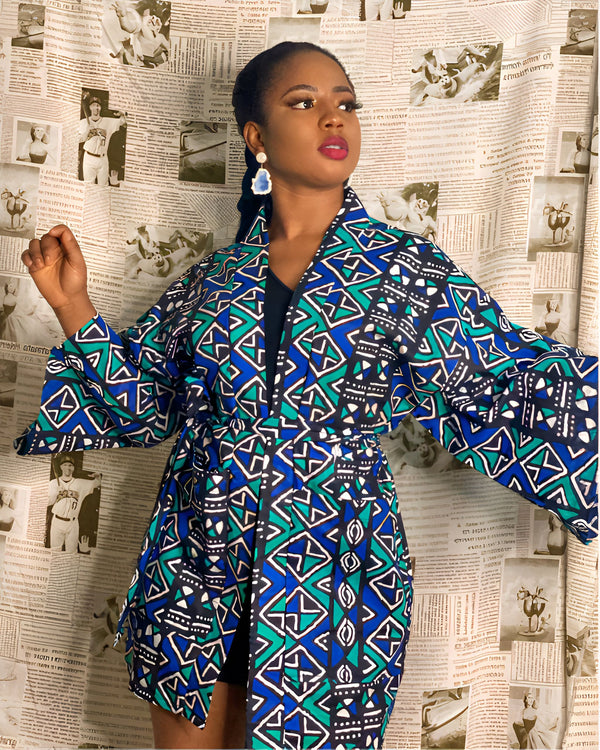 Femme portant un kimono bleu et vert avec des motifs géométriques devant un fond de journaux vintage. Parfait pour un look tendance et confortable. Découvrez notre collection de kimonos.