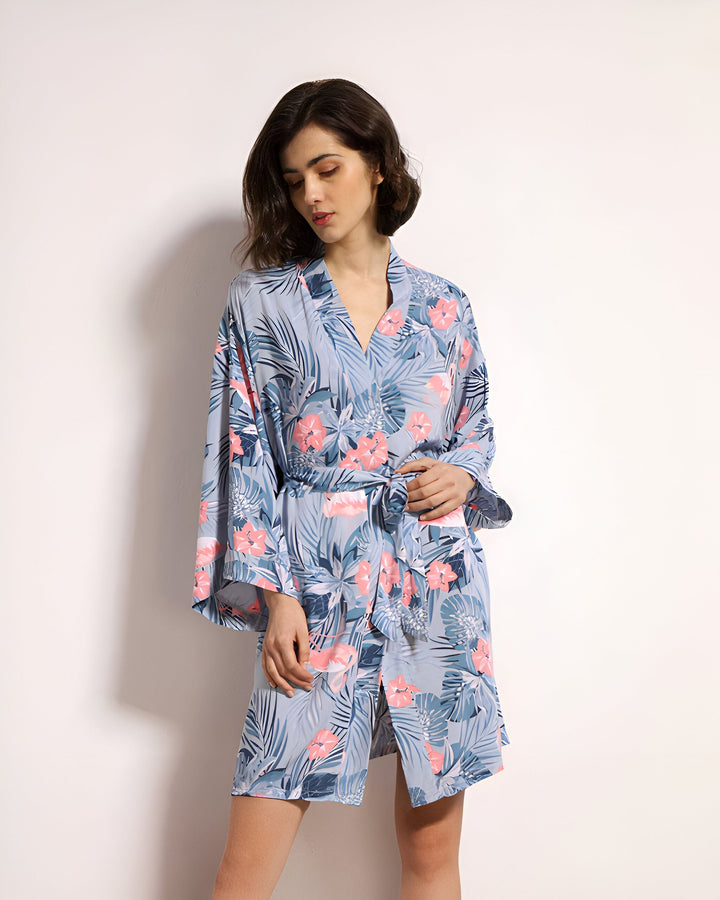 Femme portant un kimono bleu à motifs floraux roses et feuilles. Kimono de chambre élégant, parfait pour la détente. Découvrez notre collection de kimonos.