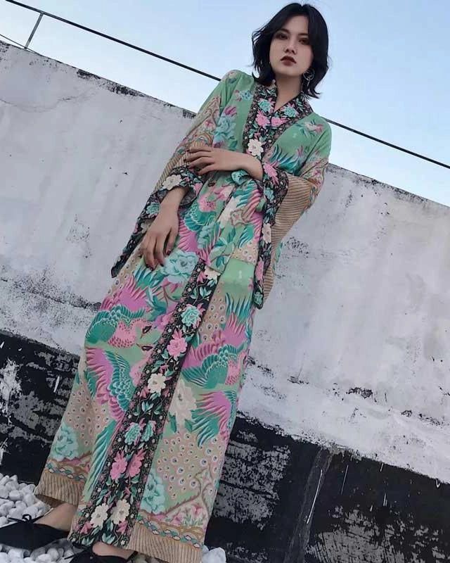 Femme portant un kimono long et fluide avec imprimé floral et paons dans les tons de vert, rose et beige. Vêtements de style japonais à la mode. Notre collection de kimonos uniques.
