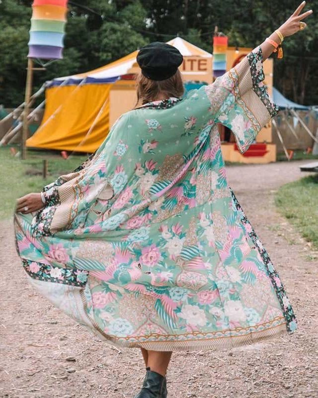 Femme portant un kimono fleuri vert et rose, dos tourné, chapeau noir. Festival en arrière-plan. Vêtements de style kimono à vendre.