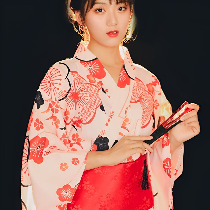 Jeune femme portant un kimono rose à motifs floraux rouges et noirs, tenant un éventail. Vêtements traditionnels japonais à vendre.