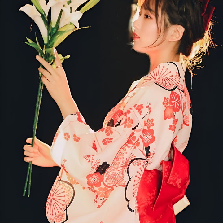Femme portant un kimono japonais traditionnel à motifs floraux rouges et blancs. Elle tient des lys blancs. Découvrez notre collection de kimonos uniques et élégants.