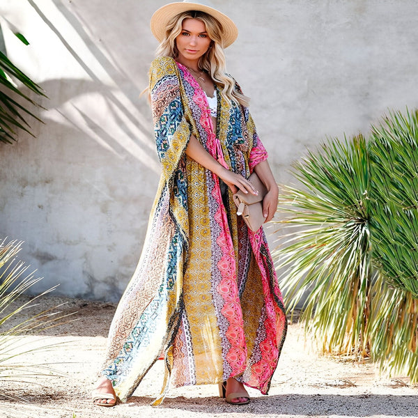 Femme blonde portant un long kimono coloré à motifs. Accessoires: chapeau de paille et pochette. Idéal pour la plage ou une tenue décontractée chic. Découvrez notre collection de kimonos pour femmes!