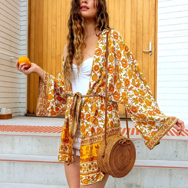 Femme portant un kimono à motifs floraux oranges et blancs, sac rond en osier, tenant une orange. Vêtements kimono tendance.