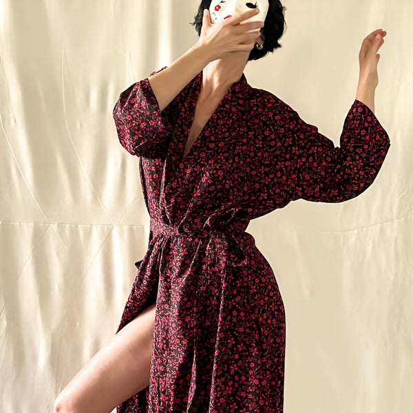 Femme portant un kimono fleuri rouge et noir, un masque blanc couvrant son visage. Idéal pour une tenue décontractée chic ou comme peignoir élégant. Découvrez notre collection de kimonos uniques !