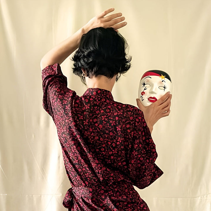 Femme de dos en kimono à motifs floraux rouges tenant un masque de geisha. Vêtements japonais traditionnels en vente.