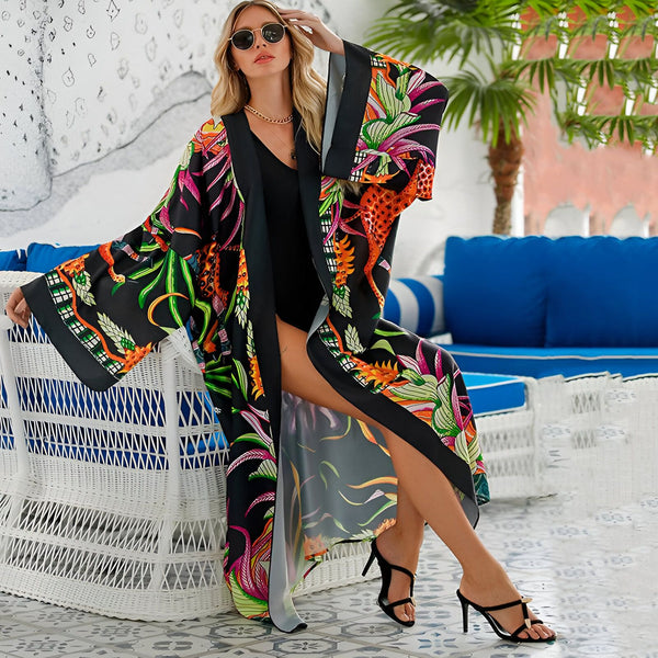 Femme portant un kimono noir imprimé de motifs tropicaux colorés, assise près d'une piscine. Kimonos pour femmes disponibles à l'achat en ligne.