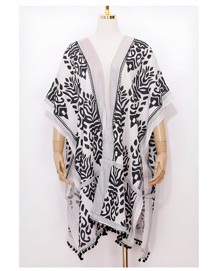 Kimono blanc à motifs noirs sur mannequin. Vêtement ample avec pompons, idéal comme tenue d'été ou de plage. Découvrez notre collection de kimonos uniques.