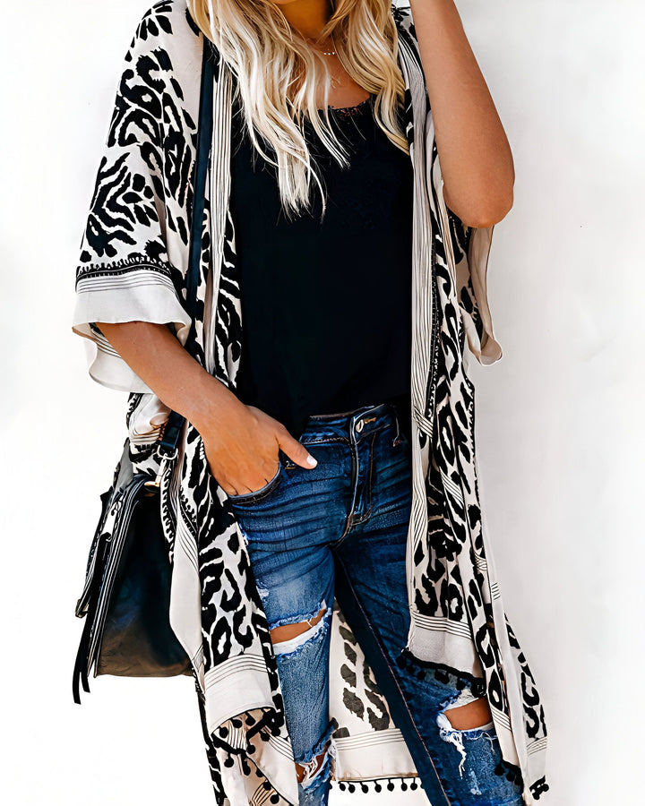 Kimono long à motif léopard noir et blanc porté sur un débardeur noir et un jean déchiré bleu. Accessoires : sac à main noir. Collection kimono.