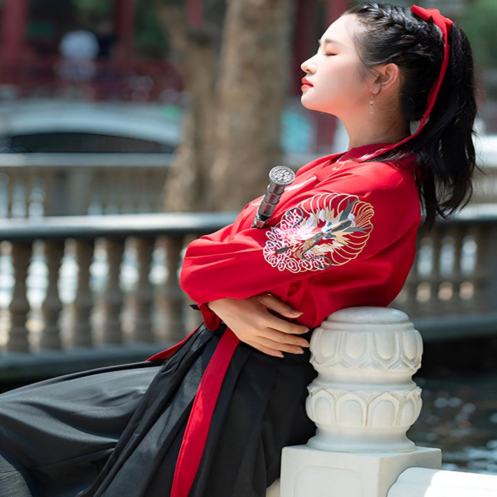 Femme portant un kimono rouge brodé avec un dragon, assise près d'un pont. Kimono traditionnel japonais de notre collection. Vêtements d'inspiration asiatique à découvrir.