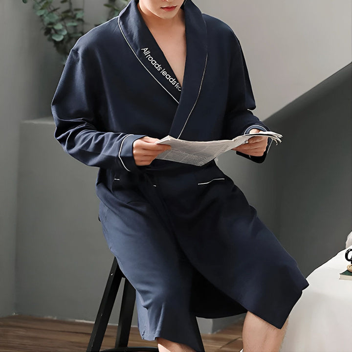 Homme en kimono bleu marine lisant journal. Peignoir kimono avec inscription brodée, style décontracté. Vêtements de nuit, détente. Boutique de kimonos en ligne.