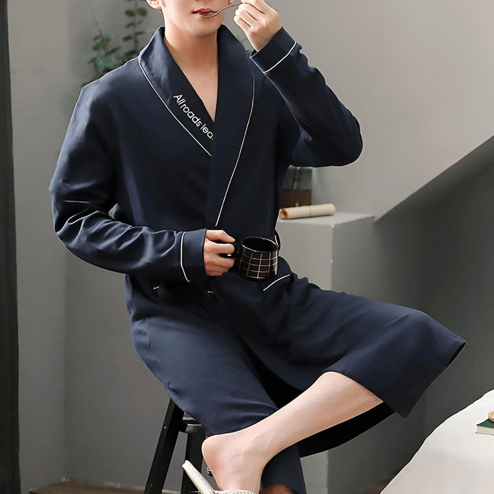 Homme en kimono bleu marine avec une tasse, savourant un moment de détente. Découvrez notre collection de kimonos élégants et confortables.