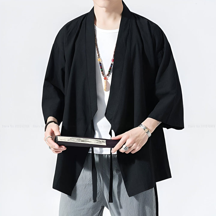 Homme portant un kimono noir, pantalon gris, tenant un éventail. Vêtements de style japonais à vendre.