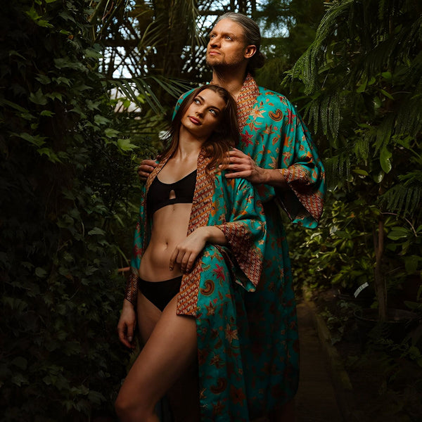 Couple portant des kimonos turquoise avec motifs floraux dans un jardin luxuriant. Vêtements de détente élégants. Collection de kimonos pour hommes et femmes.