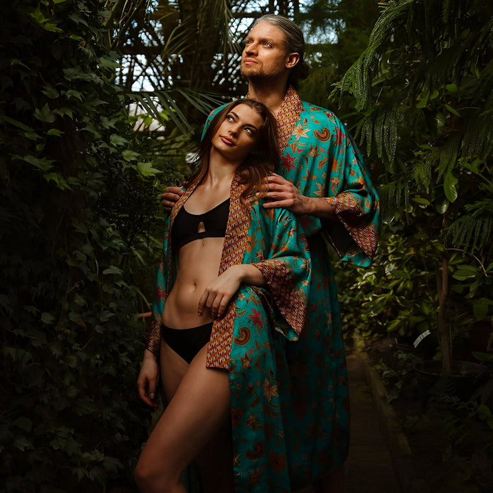 Couple portant des kimonos turquoise avec motifs floraux dans un jardin luxuriant. Vêtements de détente élégants. Collection de kimonos pour hommes et femmes.