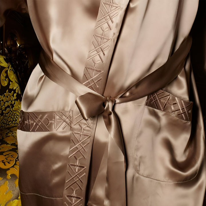 Détail d'un kimono luxueux en soie beige avec ceinture nouée. Motifs géométriques brodés sur les bords et la poche. Vêtement d'intérieur élégant et confortable.