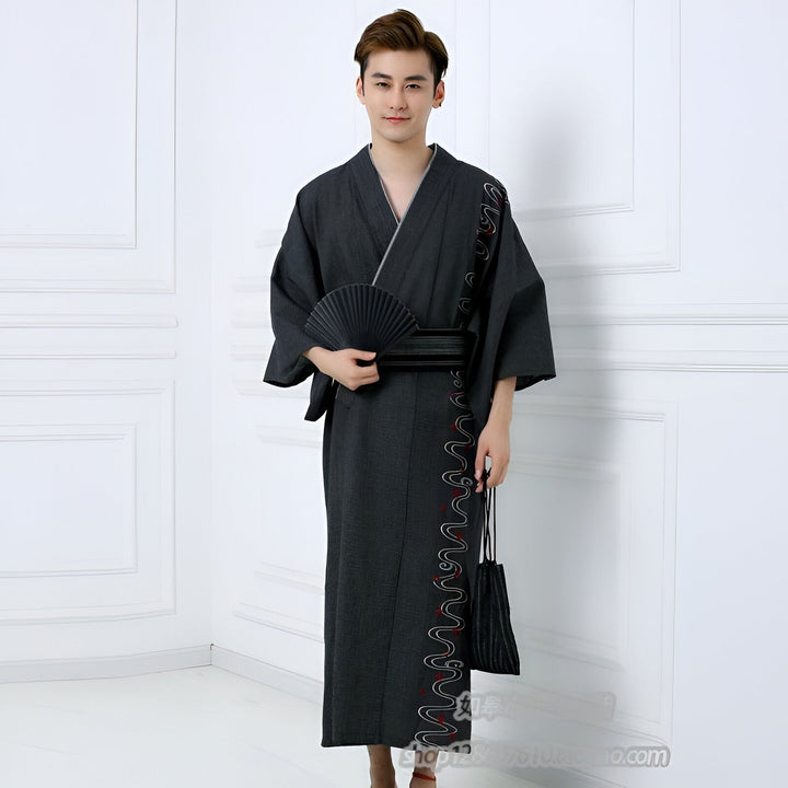 Homme en kimono japonais traditionnel noir avec motif brodé, tenant un éventail noir. Vente de kimonos pour hommes.