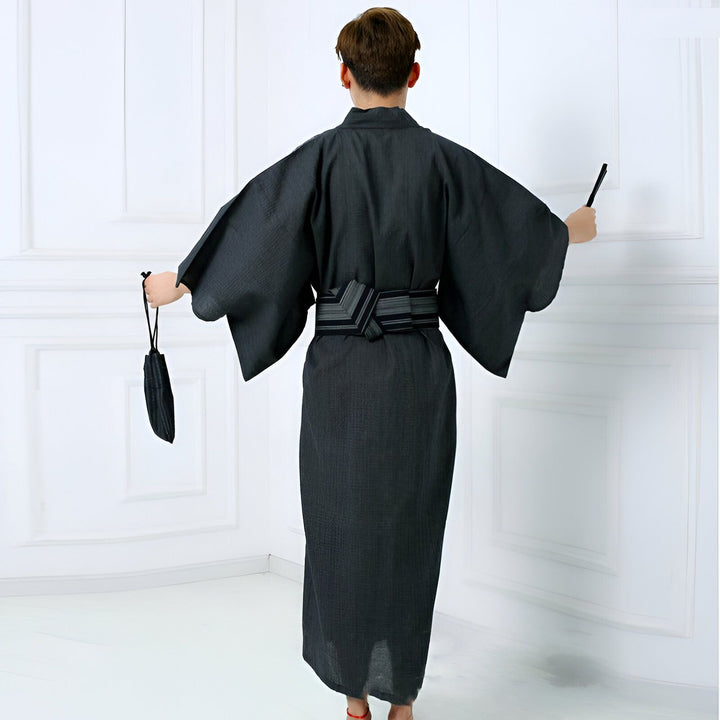 Homme portant un kimono traditionnel japonais gris foncé avec obi, vu de dos. Accessoires : sac et éventail noirs. Vêtements traditionnels, mode japonaise, kimono homme.