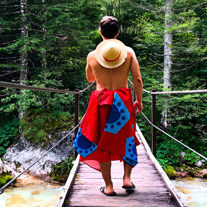 Homme vu de dos portant un kimono rouge et bleu sur un pont en bois dans la nature. Chapeau de paille sur son dos. Mode et style kimono.