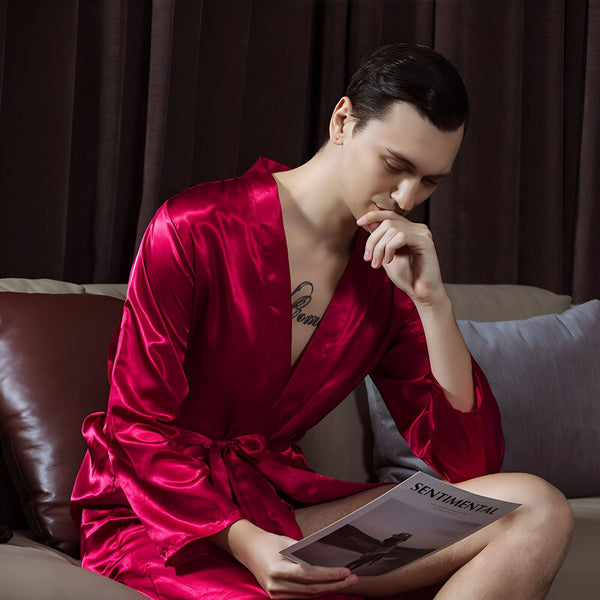 Homme portant un kimono rouge en satin, lisant un magazine. Vêtements de détente confortables et élégants. Boutique de kimonos en ligne.