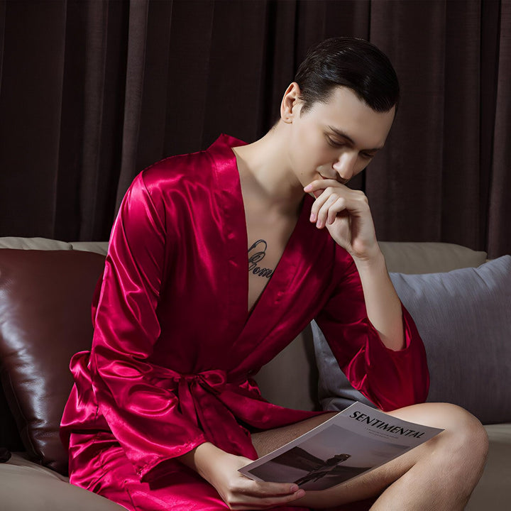 Homme portant un kimono rouge en satin, lisant un magazine. Vêtements de détente confortables et élégants. Boutique de kimonos en ligne.