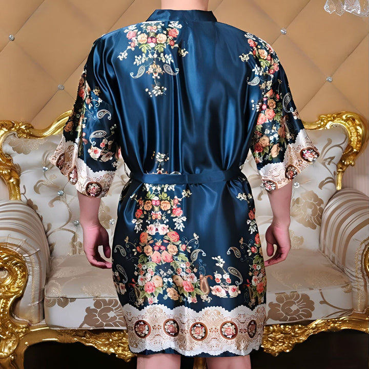 Homme portant un kimono bleu satiné avec motifs floraux. Vêtement de détente luxueux, parfait pour la maison. Découvrez notre collection de kimonos uniques.
