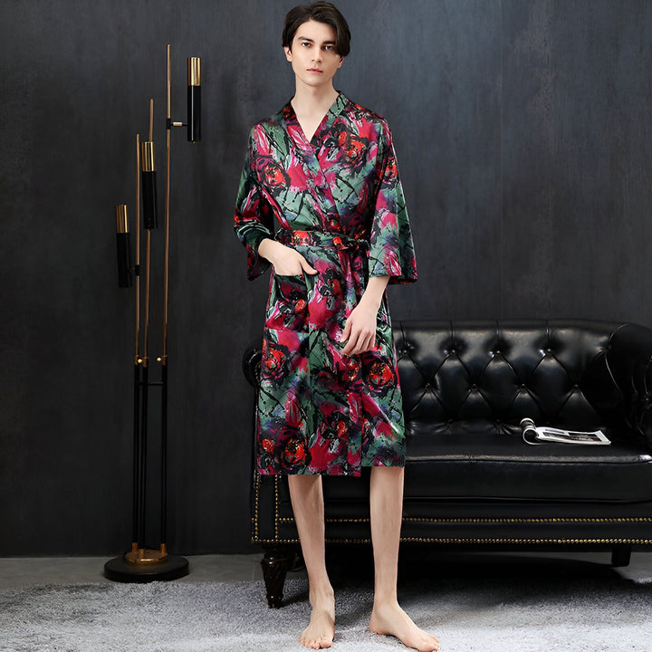Homme portant un kimono en soie à motifs floraux rouges et verts. Peignoir d'intérieur élégant avec ceinture. Vêtements de détente confortables et luxueux. Boutique de kimonos en ligne.