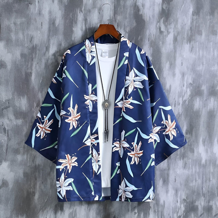 Kimono bleu marine à motifs floraux blancs et marron, suspendu à un cintre. Un t-shirt blanc et un collier pendentif complètent le look. Notre collection de kimonos pour un style unique et tendance.