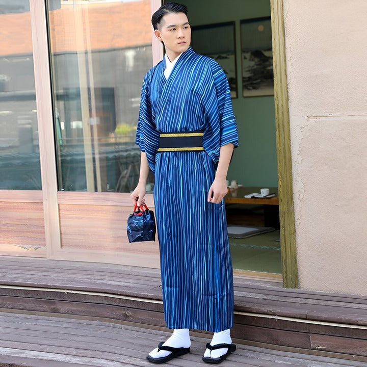 Homme portant un kimono japonais bleu rayé avec une ceinture obi noire. Il tient un petit sac bleu. Vente de kimonos traditionnels et modernes.