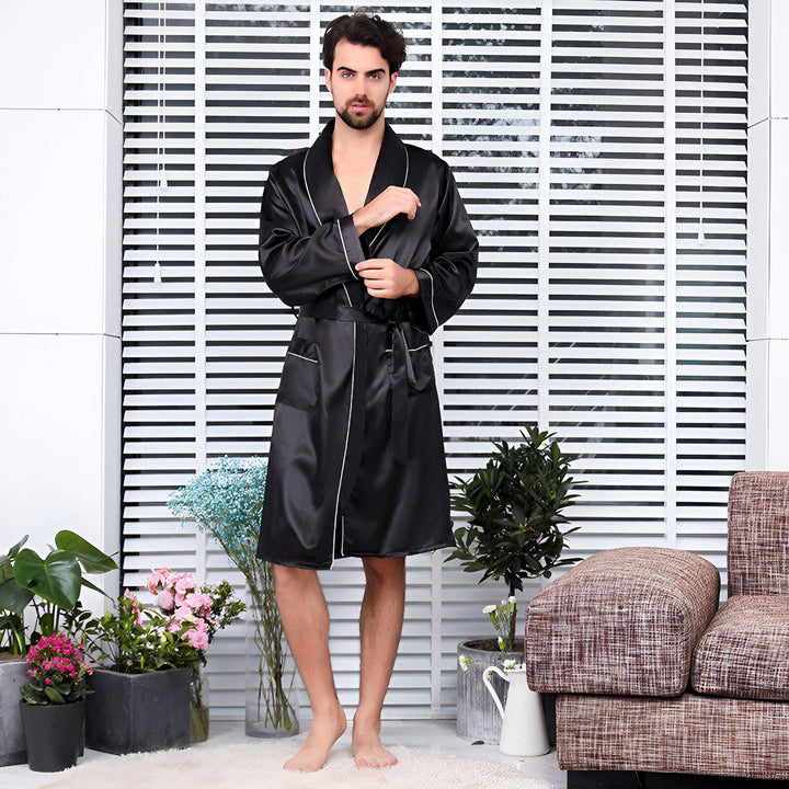 Homme portant un kimono noir de satin avec bordure blanche, idéal pour la détente à la maison. Kimonos pour hommes disponibles.