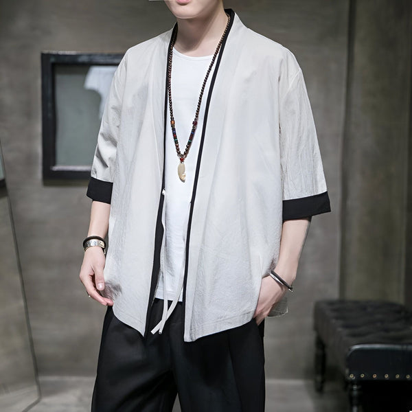 Homme portant un kimono blanc avec bordures noires. Veste style japonais décontractée, parfait pour un look moderne. Découvrez notre collection de kimonos homme.