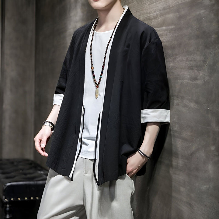 Homme portant un kimono noir à manches courtes avec bordure blanche, chemise blanche et pantalon gris. Collier à pendentif. Kimonos en vente.