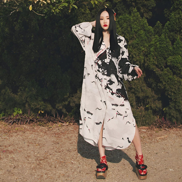 Femme portant un kimono long à motifs de grues noires et blanches. Kimono japonais traditionnel. Chaussures geta rouges et noires. Vente de kimonos en ligne.