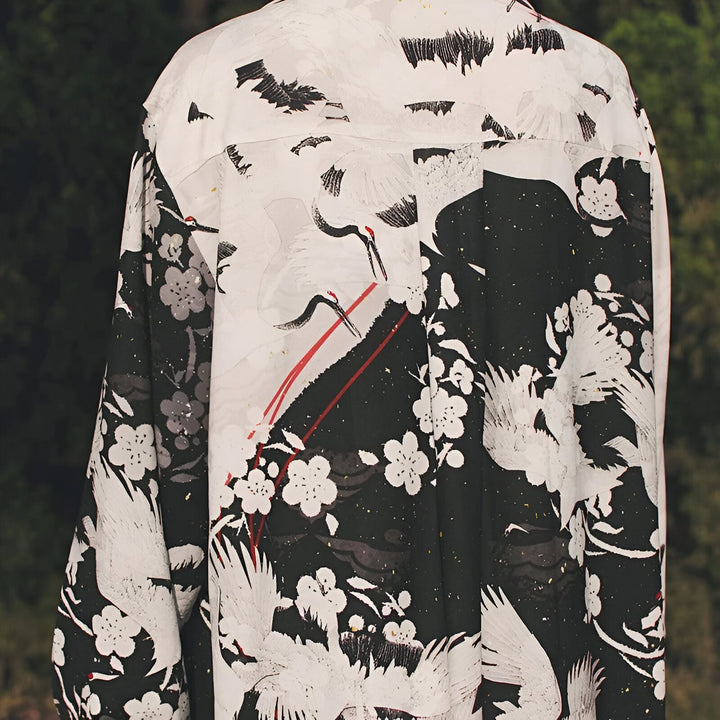 Dos d'une personne portant un kimono imprimé avec des motifs de grues blanches, de fleurs de cerisier et de motifs japonais traditionnels noirs. Kimono élégant et unique en vente.