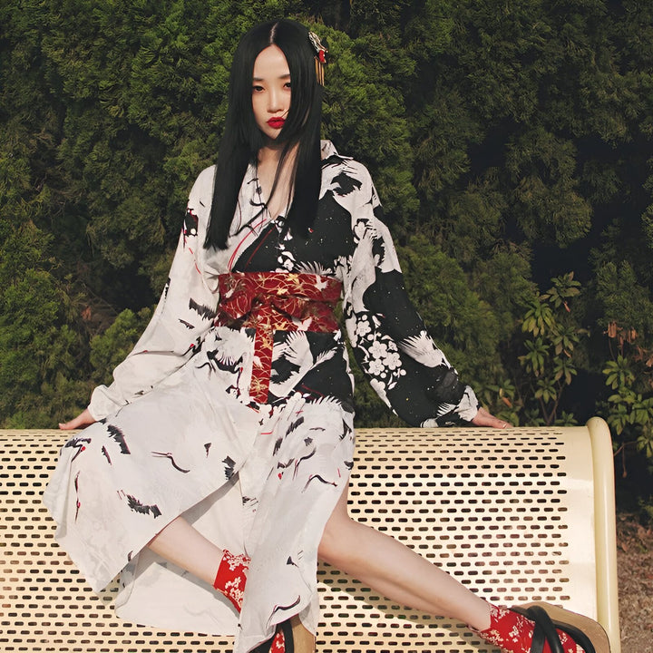 Femme portant un kimono japonais noir et blanc avec des motifs de grues et une ceinture obi rouge. Vente de kimonos traditionnels et modernes.