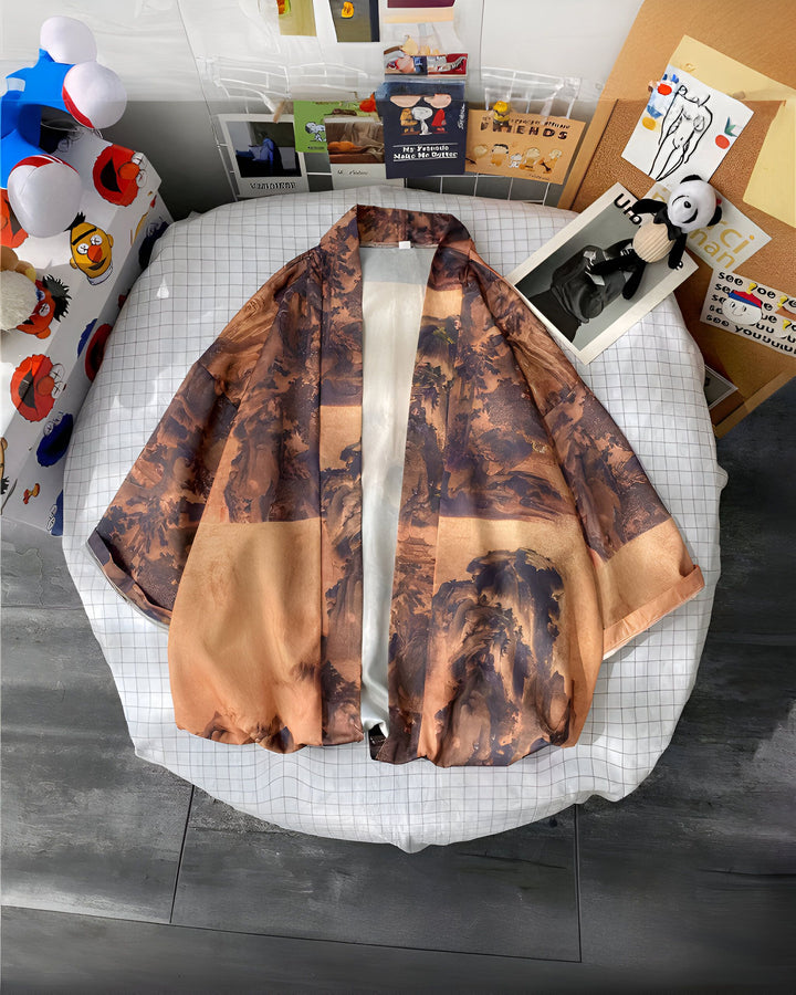Kimono marron clair avec motif de paysage montagneux, présenté sur un lit avec décorations. Vêtements kimono élégant et confortable à vendre.