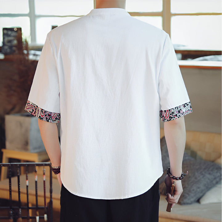 Dos d'un homme portant une chemise blanche à manches courtes avec des motifs ornementaux sur les bords des manches.