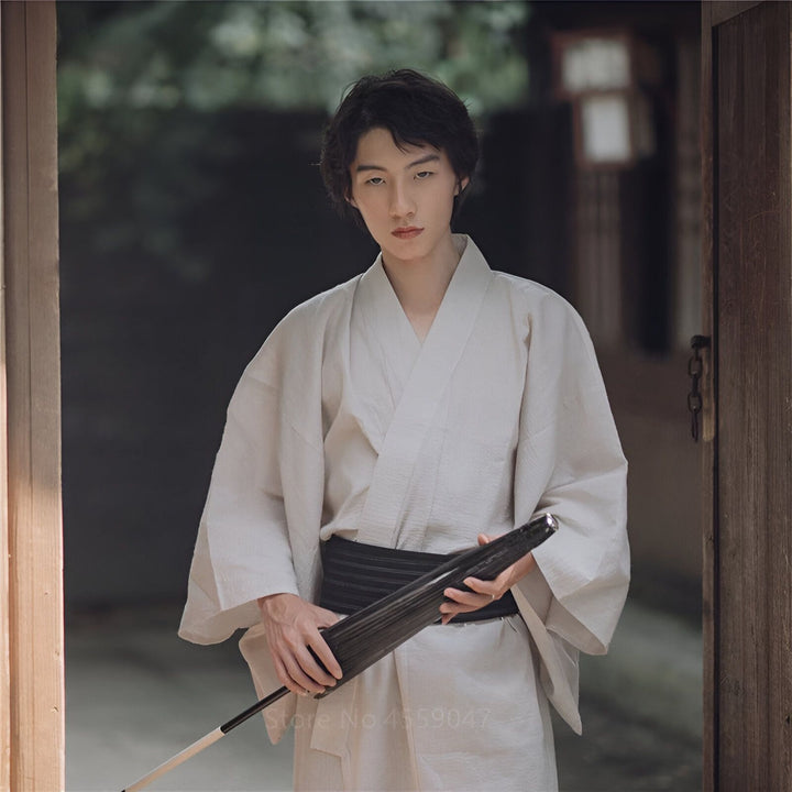 Jeune homme élégant en kimono traditionnel blanc avec obi noir, tenant un parapluie japonais. Découvrez notre collection de kimonos authentiques.