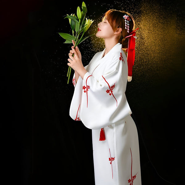 Femme en kimono blanc à motifs floraux rouges, tenant des lys. Kimonos traditionnels et modernes disponibles.