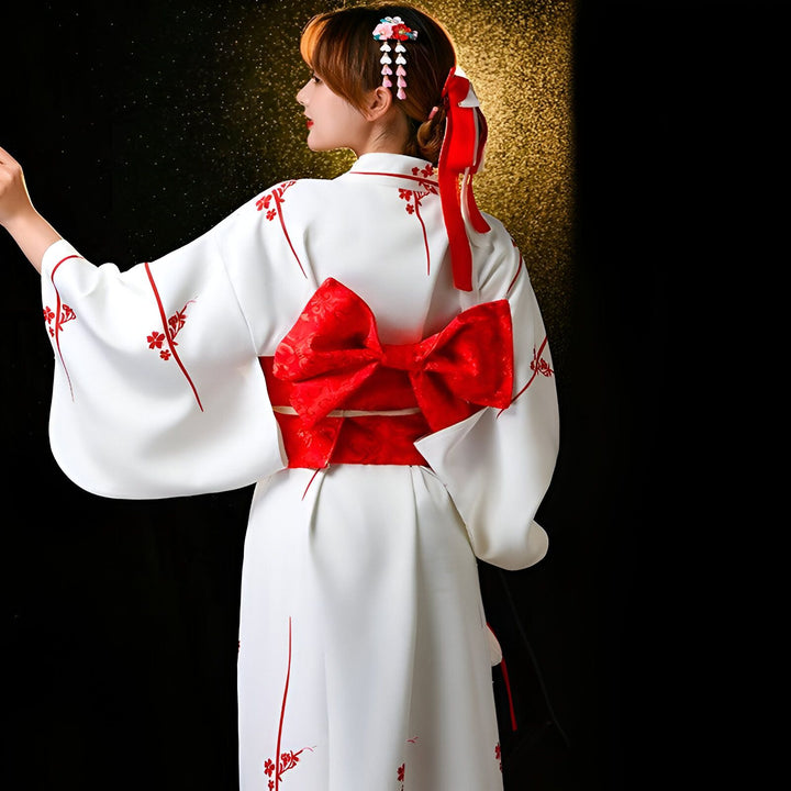Femme portant un kimono blanc orné de motifs floraux rouges, avec une large ceinture obi rouge à nœud. Kimonos à vendre.